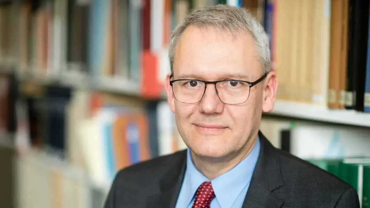 Porträt von Andreas Wirsching, der in einem Anzug und mit Brille vor einem Bücherregal steht.