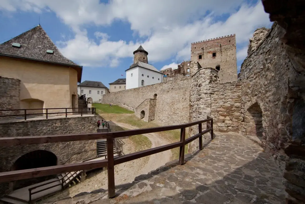 Kamienne mury i wieże zamku Stará Ľubovňa wznoszą się na tle błękitnego nieba z chmurami.