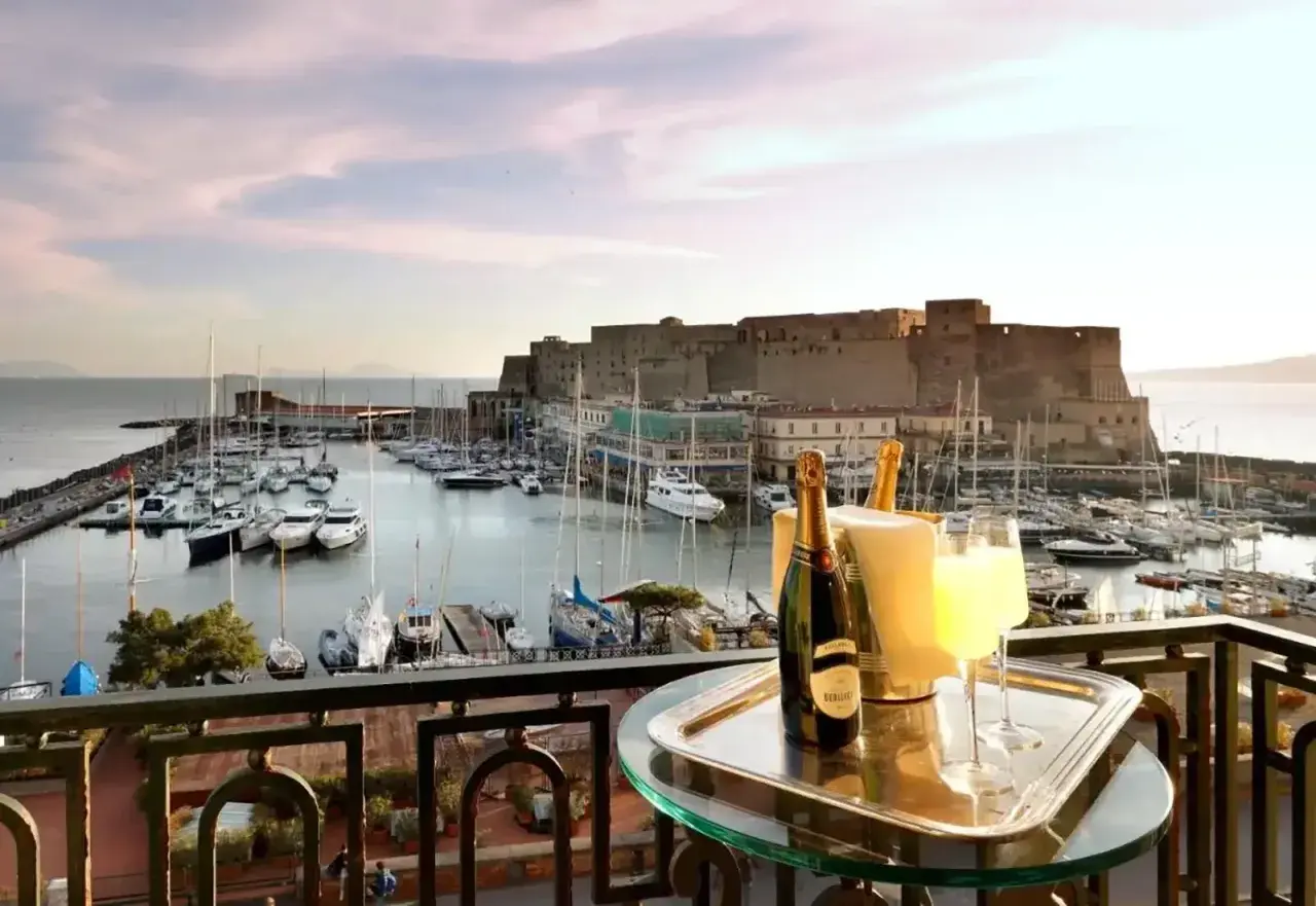 En balkong med champagne och glas, med en vy över hamnen och Castel Nuovo i Neapel.