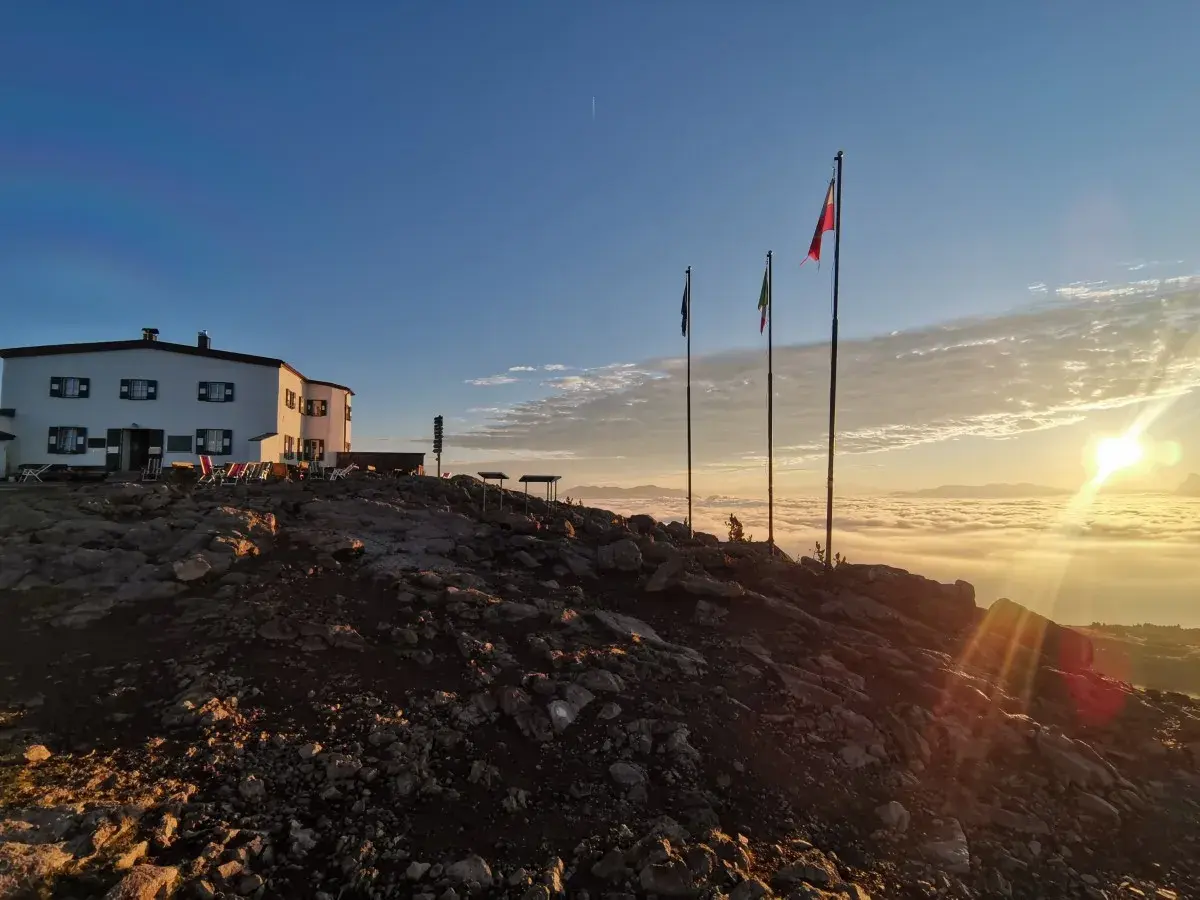Sonnenaufgang über einer Wolkendecke, mit Hütte und Fahnen. Ein perfekter Moment auf der Sarntaler Hufeisentour.
