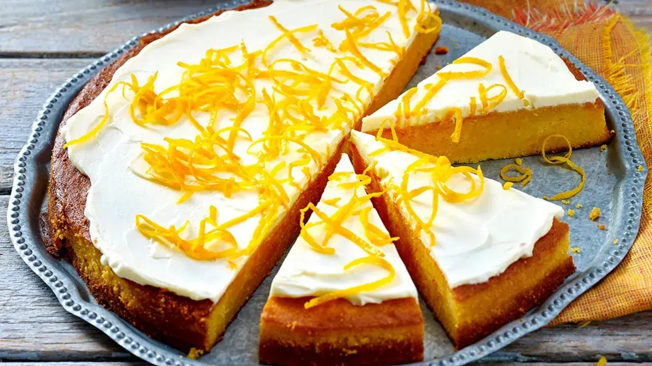 Ein saftiger, gesunder Kuchen mit weißem Zuckerguss und orangen Zesten verziert, auf einem silbernen Blech.