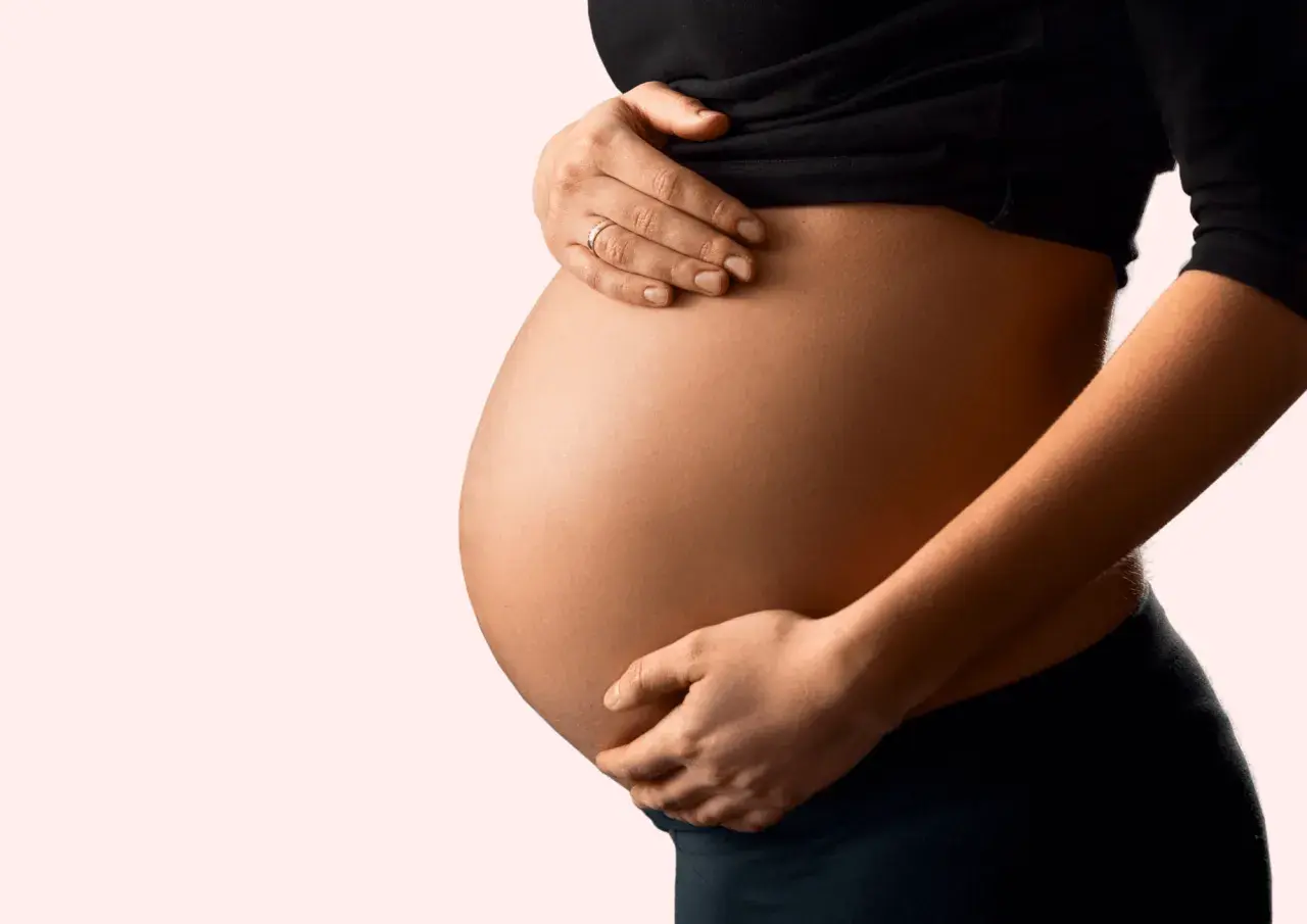 Schwanger und besorgt wegen eines Bandscheibenvorfalls? Die Hände einer Frau stützen sanft ihren runden Bauch.