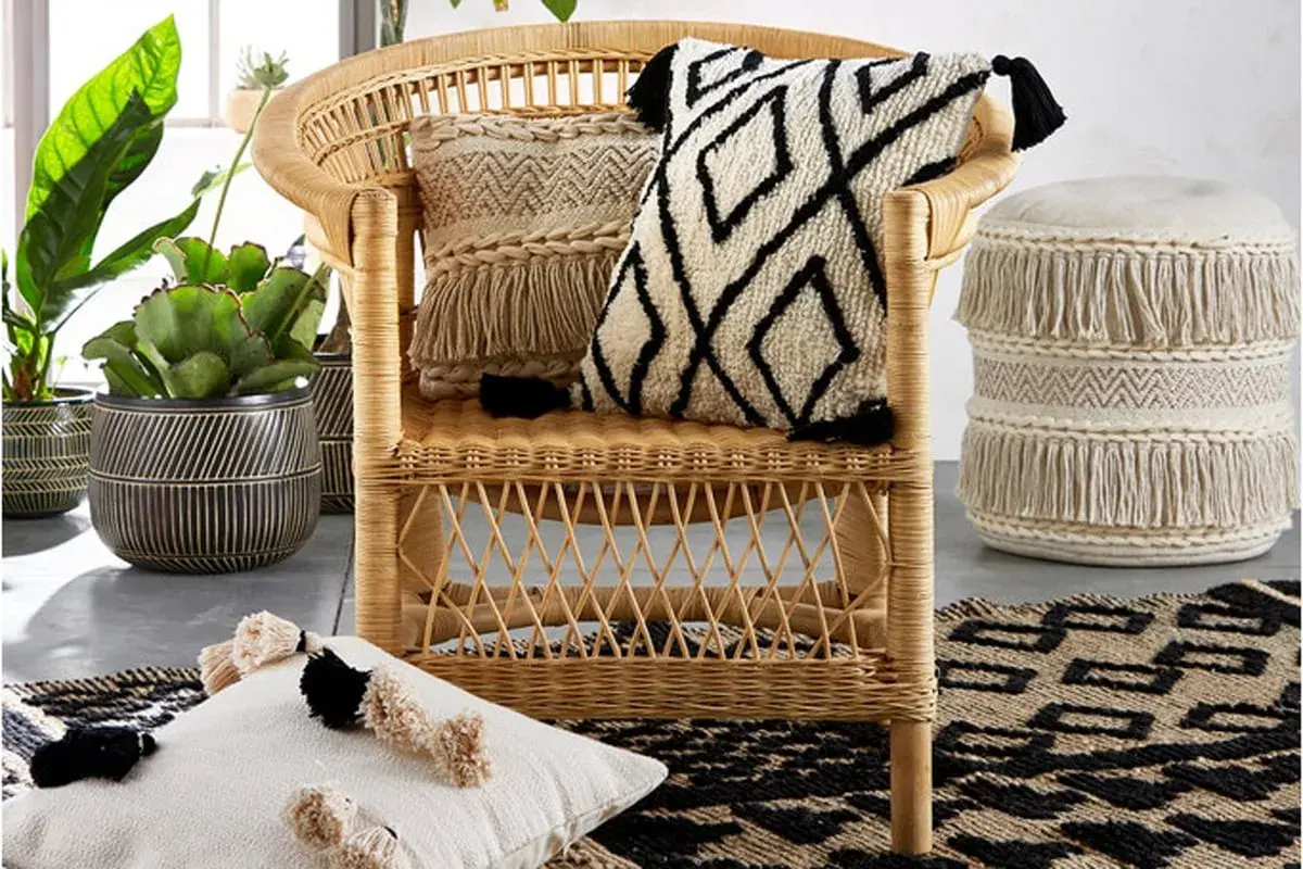 A rattan chair with decorative pillows and a fringed pouf, showcasing various types of fancy chairs and bohemian decor.