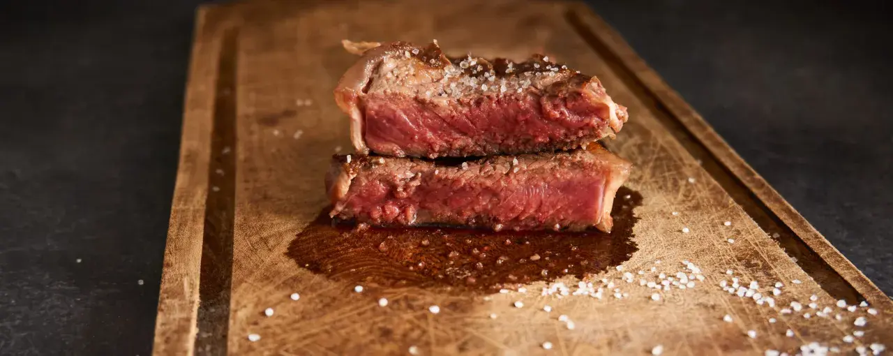 Filet mignon coupé en deux, saignant et parsemé de gros sel sur une planche en bois. Parfait pour une recette filet mignon moelleux.