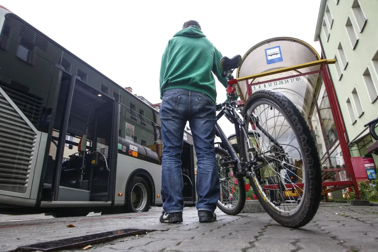 Mężczyzna z rowerem czeka na autobus. Rower stoi obok niego przy przystanku.