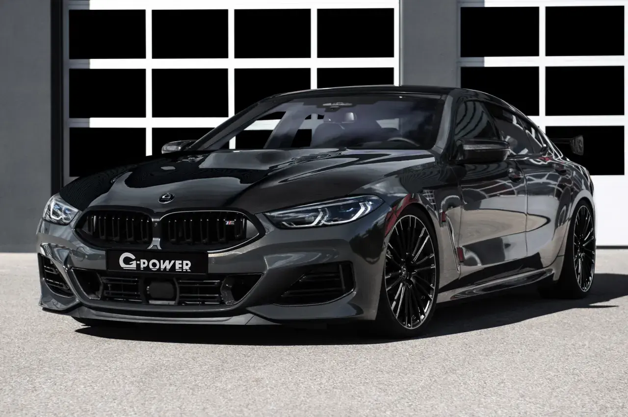 Ein getunter BMW M850 Gran Coupé in dunklem Grau mit Carbon-Elementen und auffälligem Heckspoiler steht vor einer Garage.