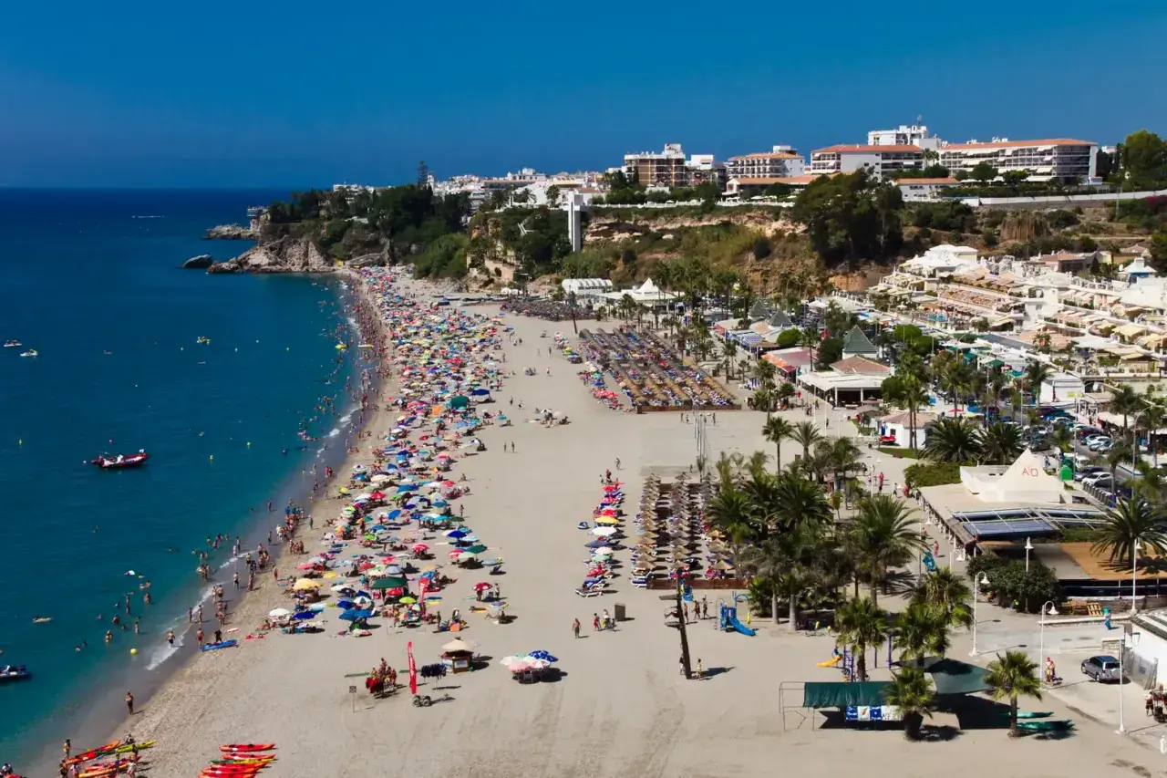 Vista aérea de la bulliciosa playa de Burriana, considerada la mejor playa de Nerja, con gente disfrutando del sol y el mar azul.