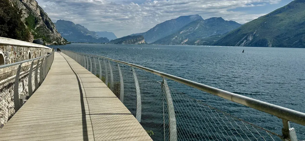 Drewniana promenada nad jeziorem Garda, z widokiem na góry i żaglówki. Idealne miejsce na spacer po mieście.