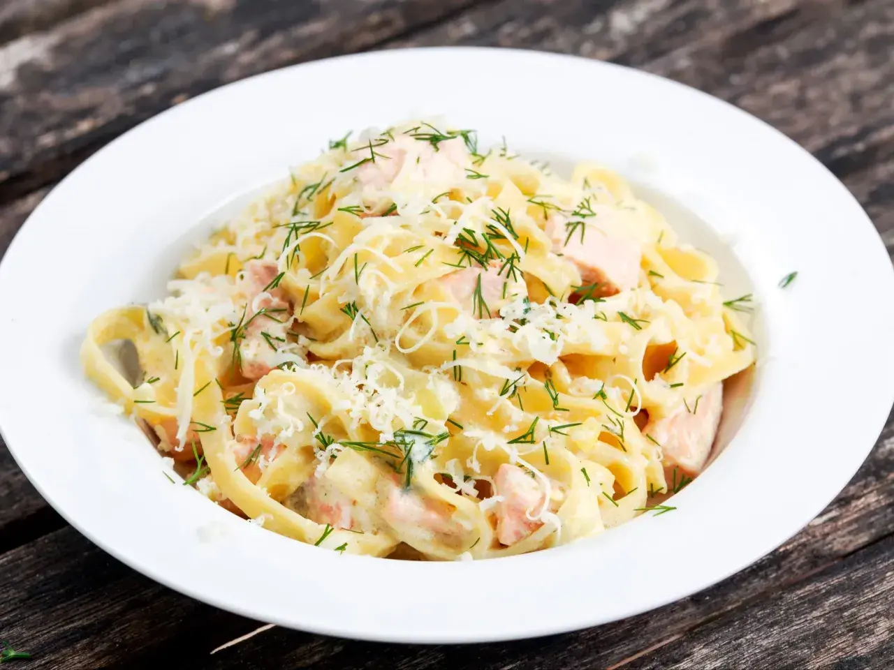 Pyszne fettuccine z łososiem w kremowym sosie, posypane parmezanem i świeżym koperkiem. Idealne danie dla miłośników ryb.