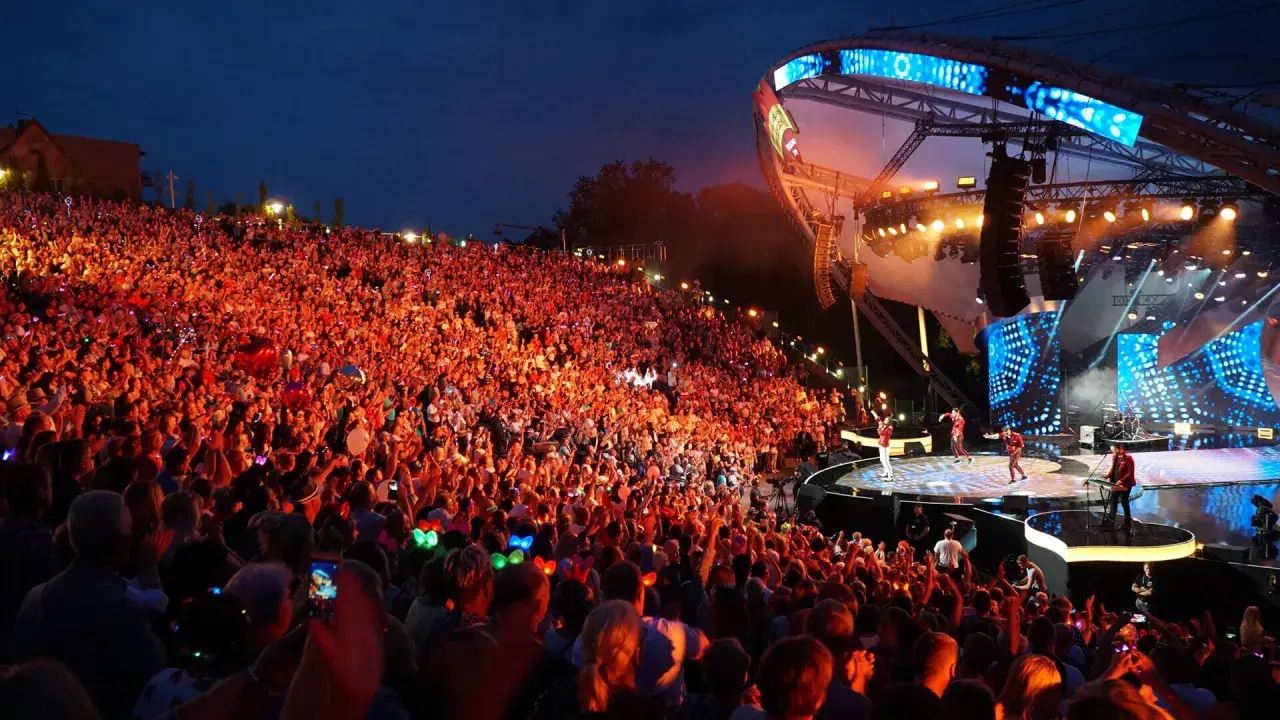 Tłumy rozbawionych ludzi na mrągowo festiwal, oświetlone sceną i kolorowymi światełkami.