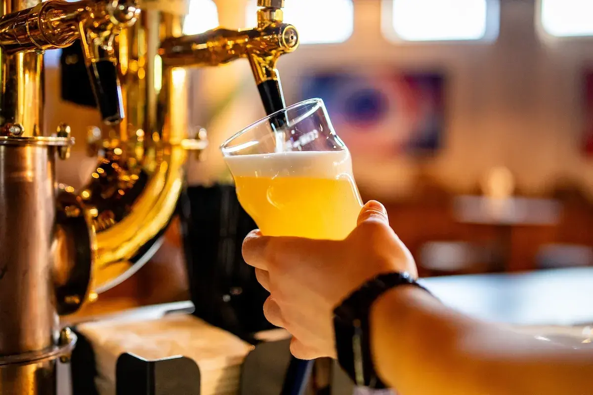 Hand holding a glass of beer being poured from a golden beer tap.