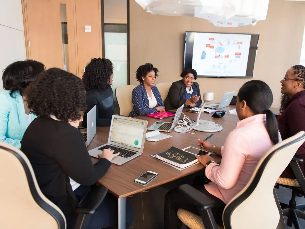 A diverse team collaborates in a meeting room, with one woman acting as an internal coach, guiding the discussion.