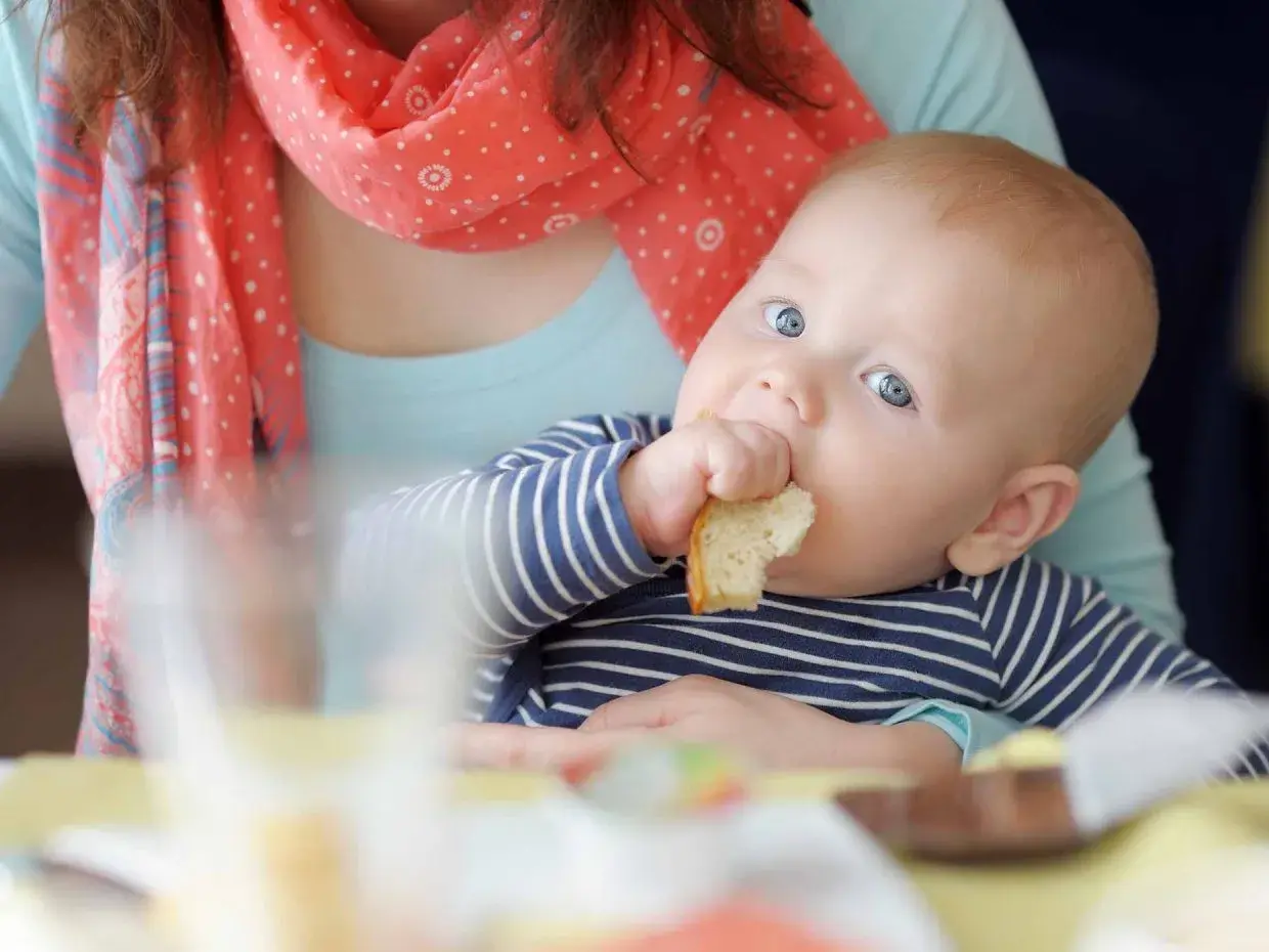 Bambino con occhi azzurri assaggia un pezzo di pane, un momento chiave per capire quando iniziare lo svezzamento.