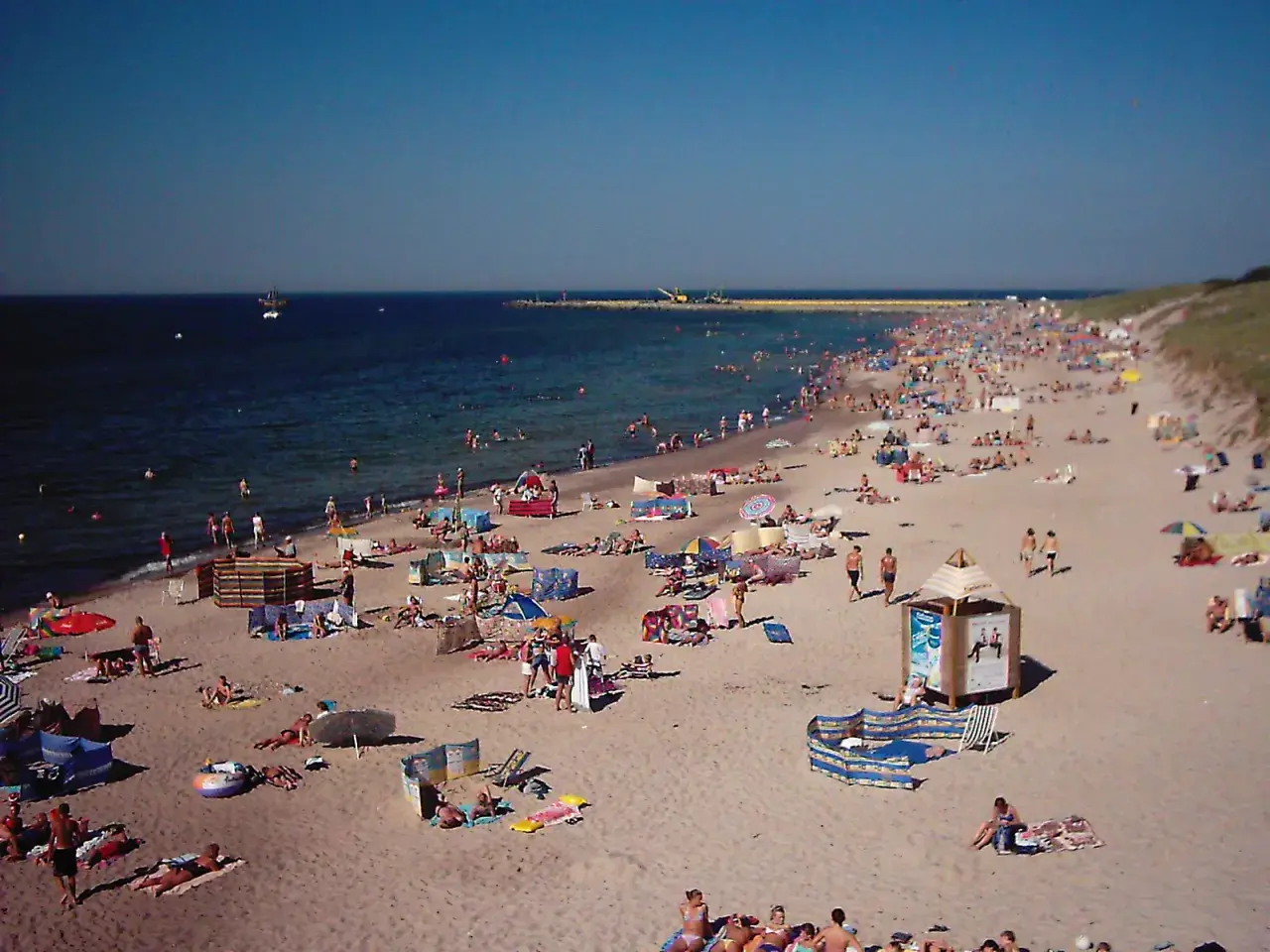Tłum ludzi wypoczywa na plaży w Darłówku. Słońce, morze i piasek tworzą idealne warunki do relaksu.