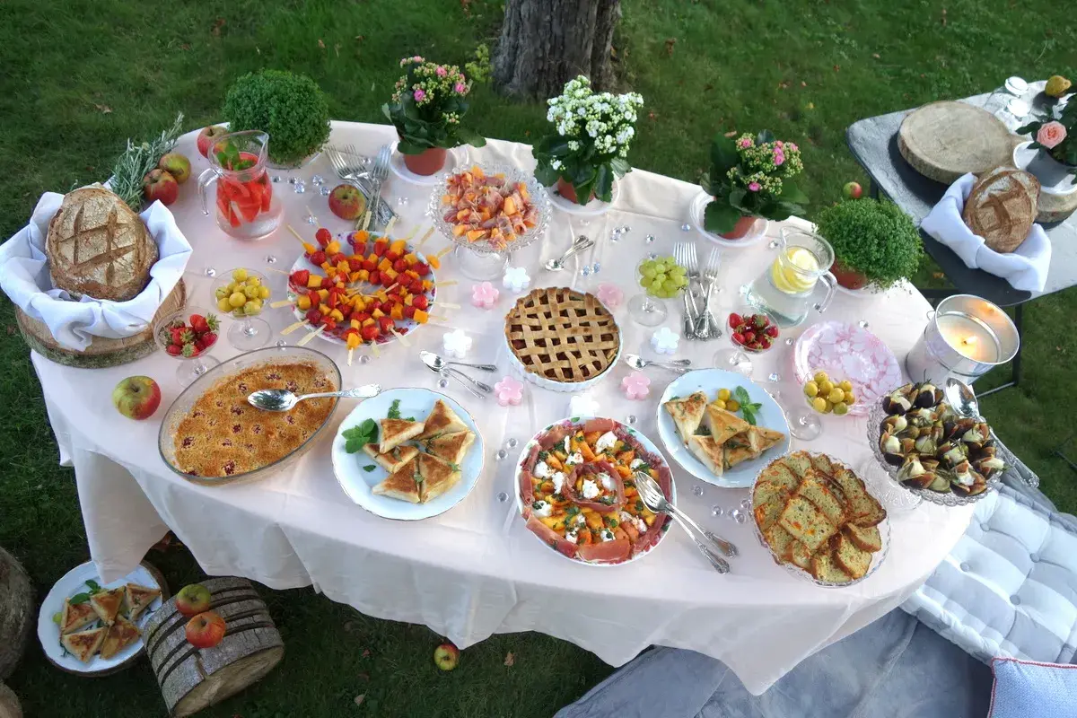 Un magnifique buffet pour une idée pique-nique : tartes, brochettes de fruits, salades, pain et boissons rafraîchissantes sur une table dressée en extérieur.