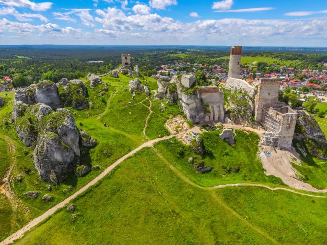 Ruiny zamków na wapiennych skałach w **parku krajobrazowym Orlich Gniazd**. Zielone wzgórza i błękitne niebo.