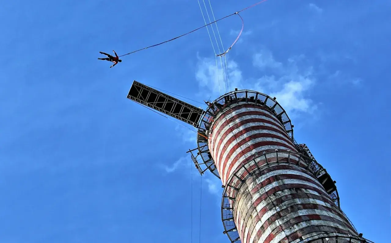 Osoba skacze na bungee z wieży, doświadczając adrenaliny. To najwyższe bungee w Polsce, oferujące niezapomniane wrażenia.