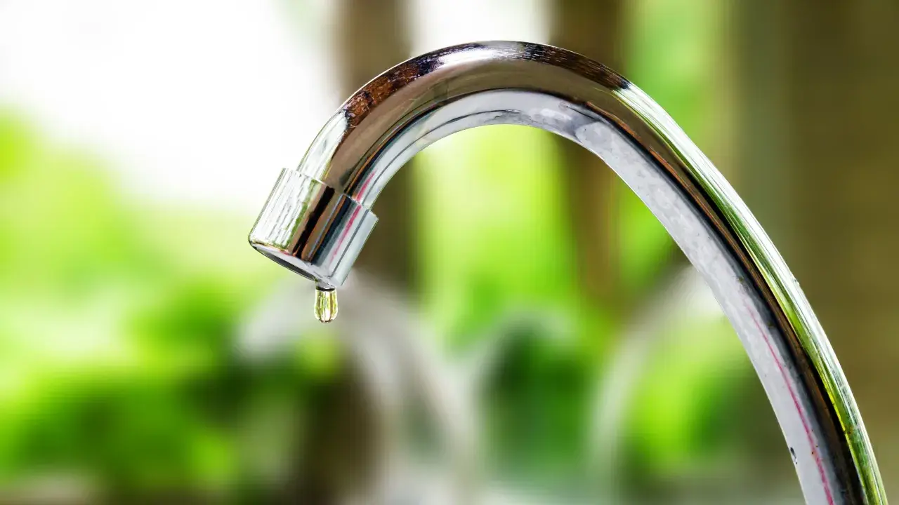Close-up of a dripping chrome faucet with a water droplet forming.