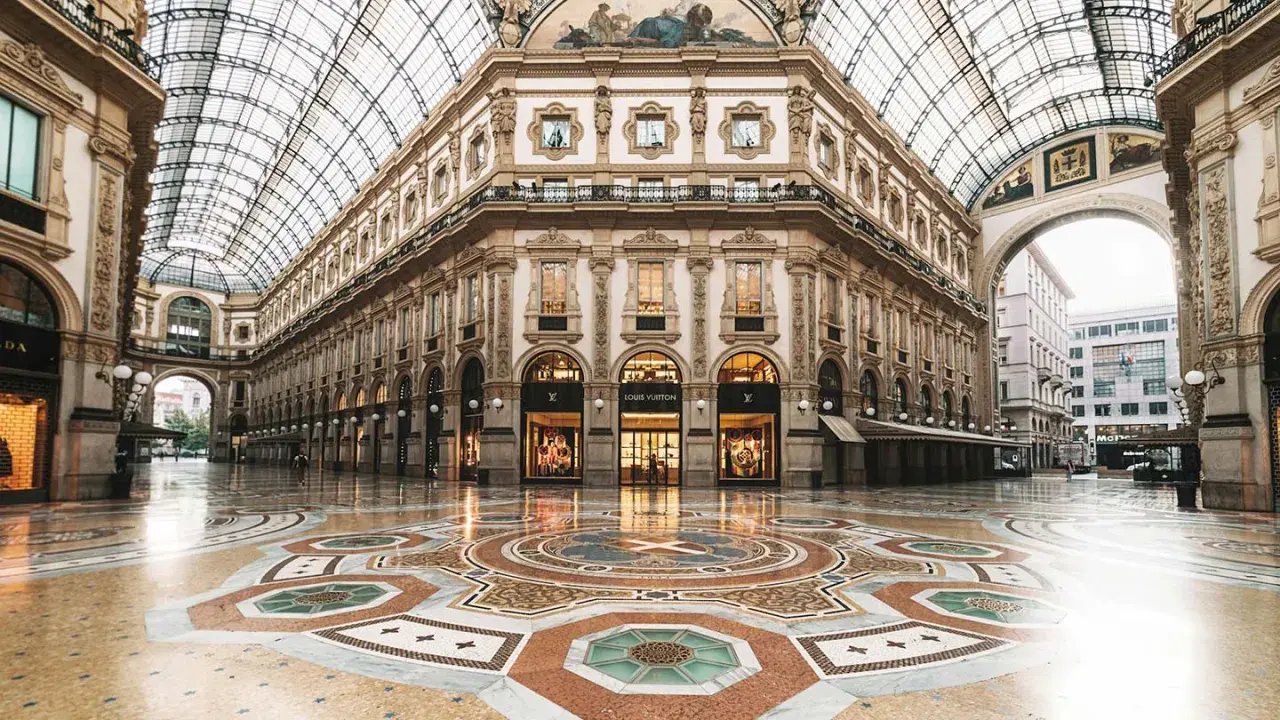 Ett tomt, lyxigt modehus i Milano med en vacker mosaikgolv och glastak. Louis Vuitton-butiken lyser upp.