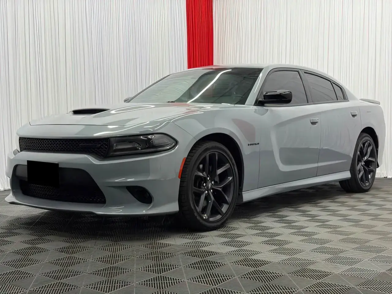 Szary Dodge Charger Hellcat z czarnymi felgami i przyciemnianymi szybami stoi na kratkowanej podłodze.