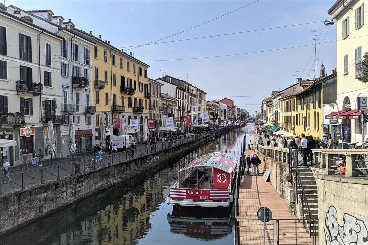 En båt på Navigli i Milano, omgiven av färgglada byggnader och folk som promenerar längs kanalen.