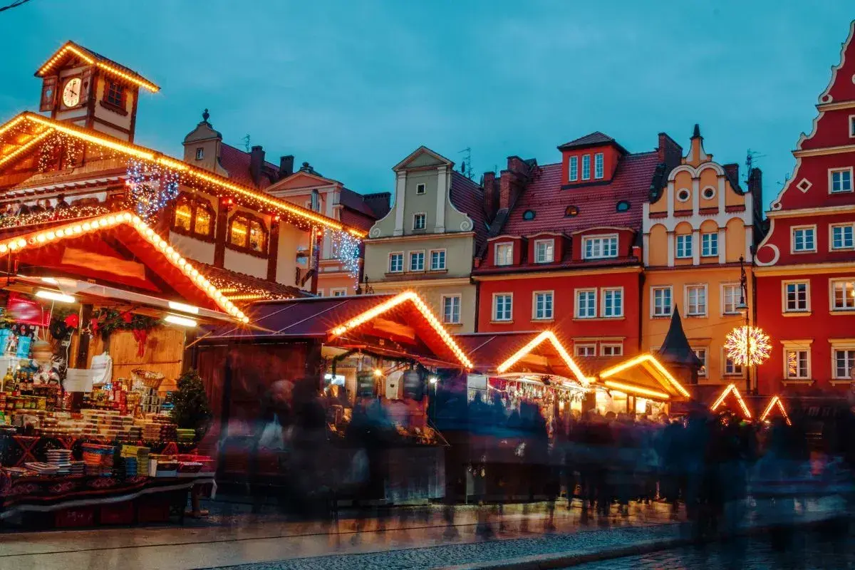Bunte Häuser und beleuchtete Stände auf dem Wroclaw Weihnachtsmarkt. Menschen schlendern durch die festliche Atmosphäre.