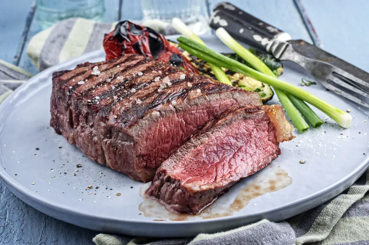 Un pavé de rumsteak grillé, coupé en tranches, servi avec des légumes rôtis et des oignons verts.
