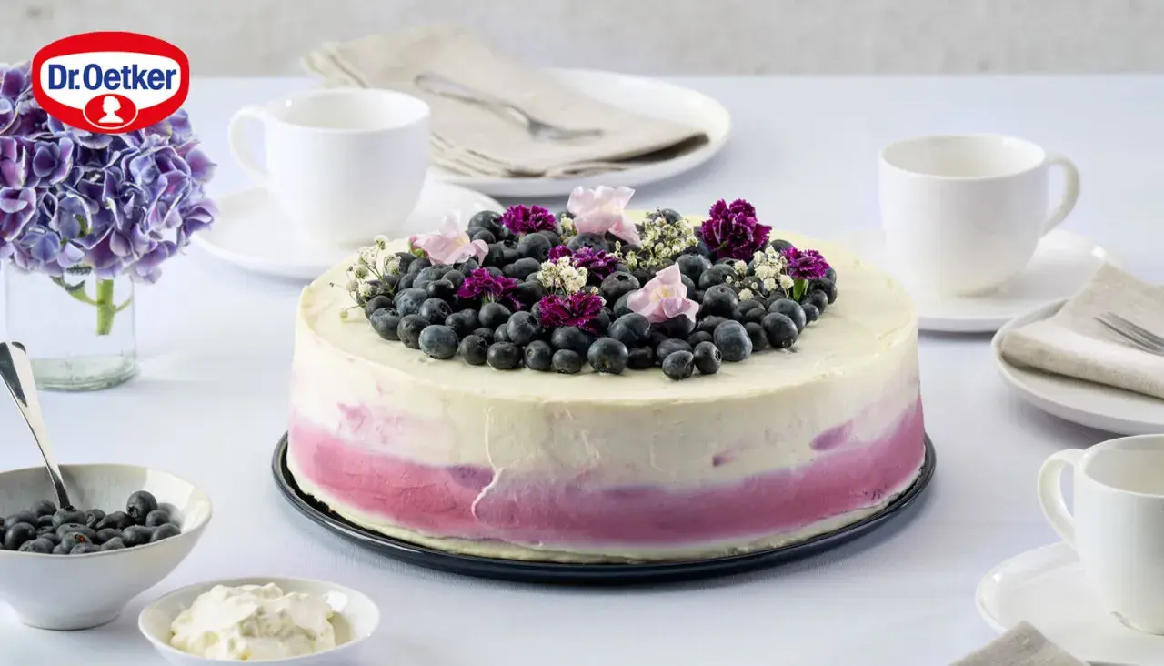 Eine wunderschöne Heidelbeertorte mit Joghurt-Frosting, garniert mit frischen Beeren und Blüten.