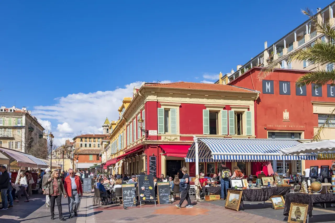 En livlig marknad i en nice gamla stan med färgglada byggnader, uteserveringar och folk som strosar.