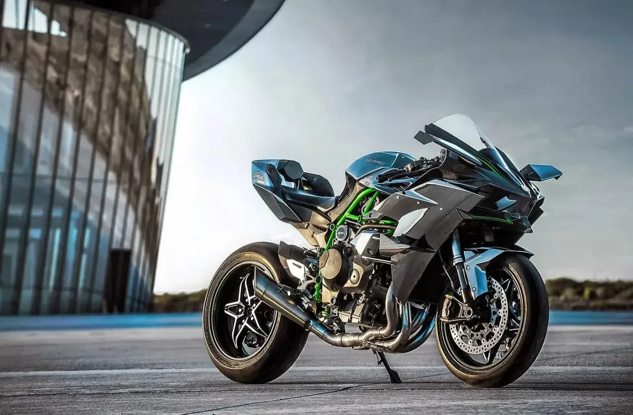 Czarny Kawasaki Ninja H2R, znany jako najszybszy motor na świecie, z zielonymi akcentami, stoi przed nowoczesnym budynkiem.