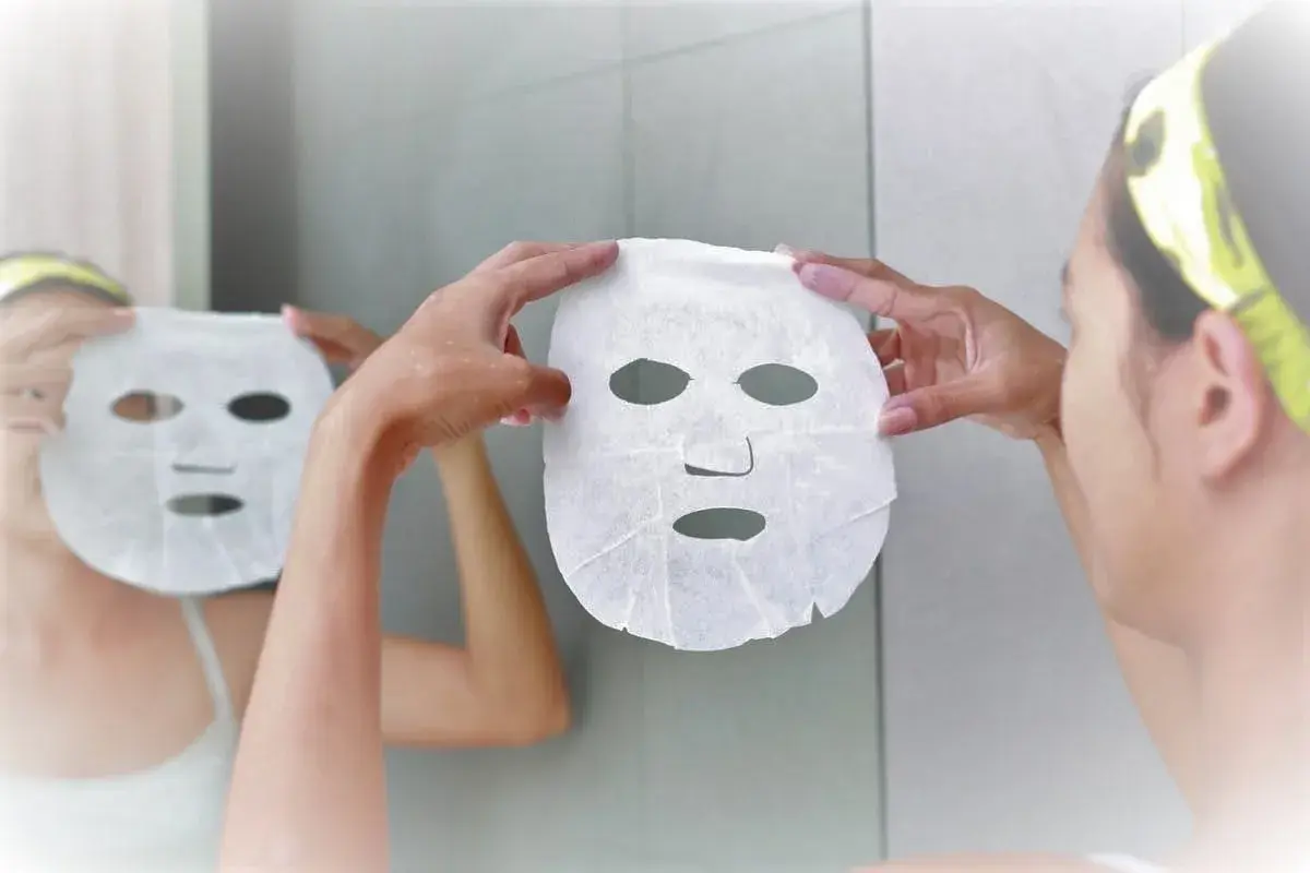 Una donna si prepara per una maschera viso, riflettendosi allo specchio. Scopri quando farla per una pelle radiosa.