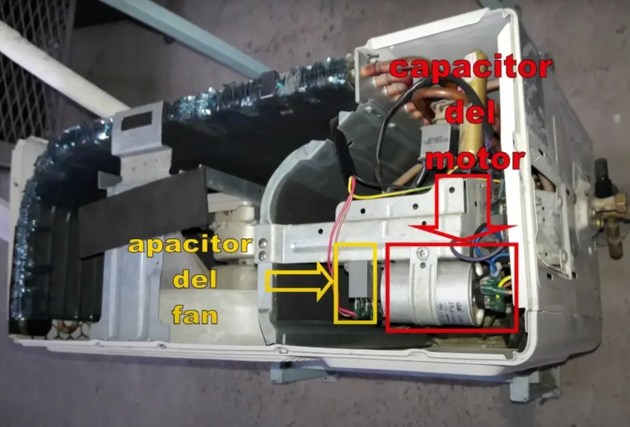 Componentes internos de un aire acondicionado, mostrando el capacitor del motor y el capacitor del fan.