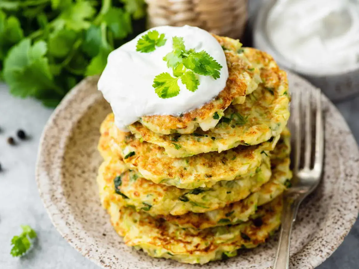 Pile de beignets de courgettes à l'italienne, garnis d'une cuillère de crème et de coriandre fraîche. Un délice croustillant et savoureux.