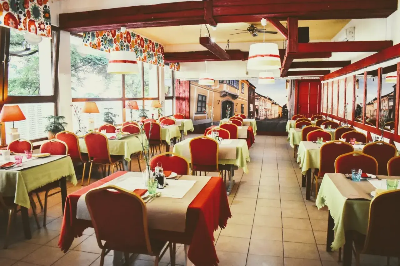 Wnętrze restauracji z czerwonymi krzesłami i stolikami nakrytymi na przyjęcie. Mural z ulicą przypomina czardasz Gdańsk.