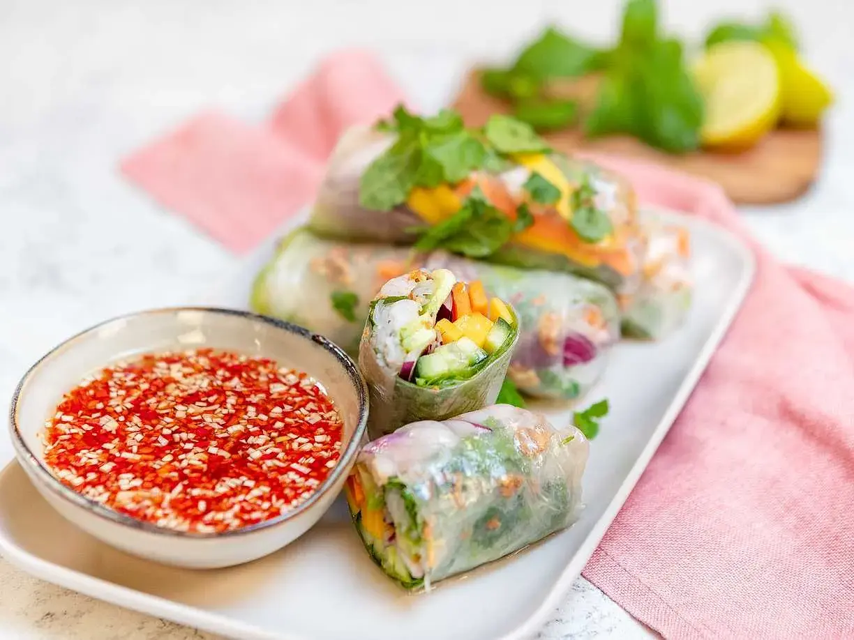 Färska vietnamesiska vårrullar fyllda med grönsaker och räkor, serverade med en röd dippsås.