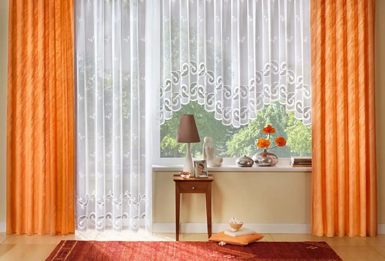 Orange und weiße Gardinen formen ein gemütliches Fensterbild. Zarte Muster zieren die weißen Stoffe, während die orangefarbenen Vorhänge Wärme ausstrahlen.