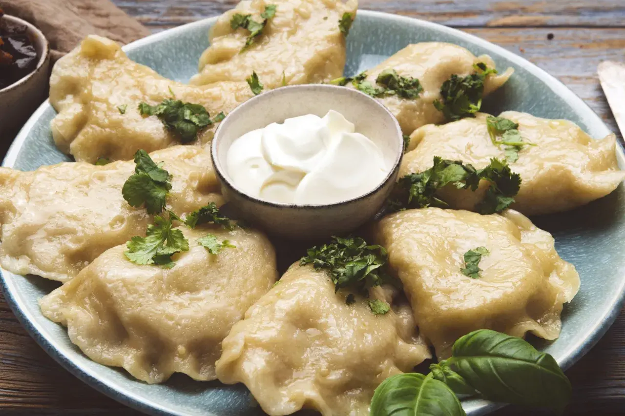 Pyszne pierogi ze szpinakiem i serem feta, udekorowane natką pietruszki, podane z kleksem śmietany.