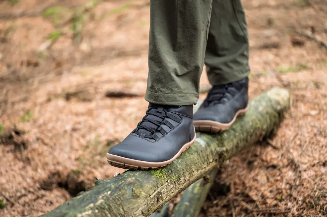 Black, low-profile shoes with tan soles, perfect as shoes to wear in winter besides boots, balance on a mossy log in a forest.