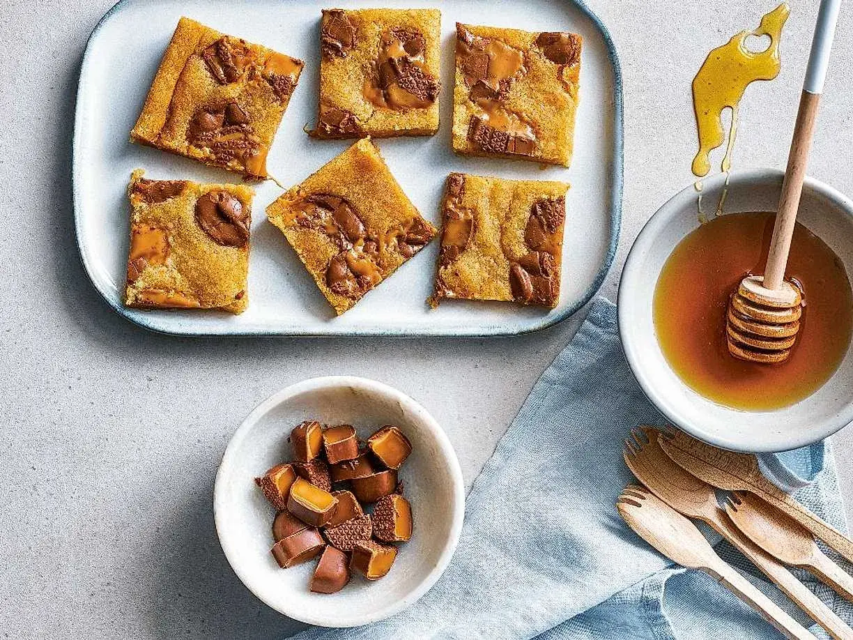 Enkla dumlekakor med chokladbitar på en bricka, bredvid en skål med honung och en skål med hackade dumlekolor.