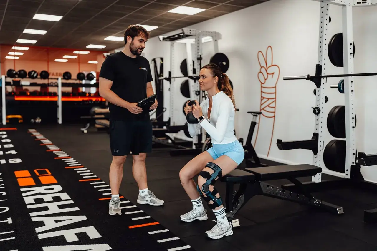 Mann mit Tablet beobachtet Frau beim Kniebeugen-Training mit Kettlebell. Meniskus Training statt OP ist hier das Ziel.