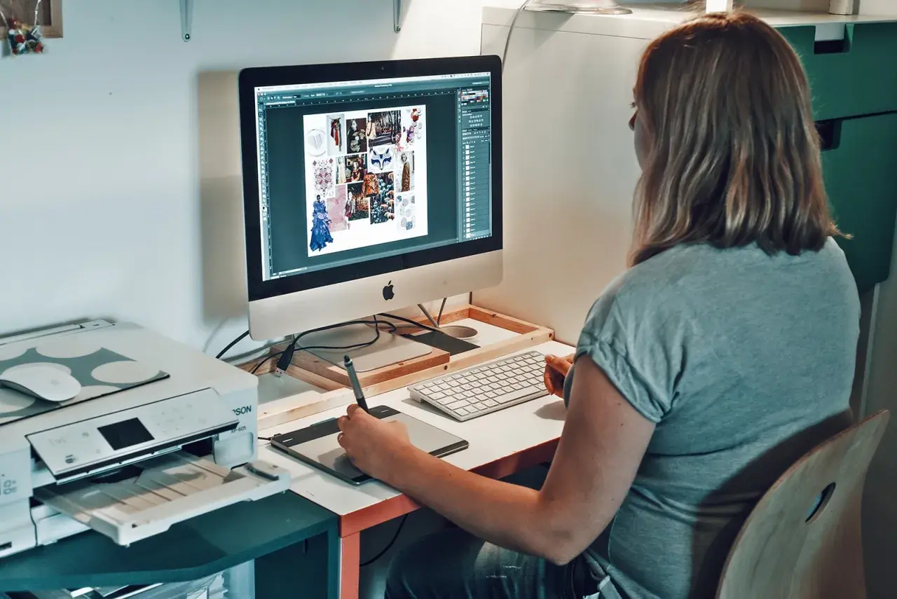 Une graphiste textile travaille sur son ordinateur, créant des moodboards et des designs. Une imprimante est visible à côté.