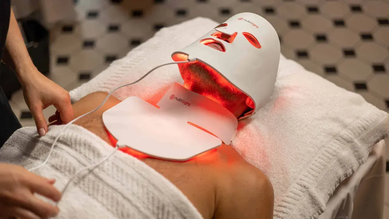 En person får behandling med en vit led mask ansikte som lyser rött.