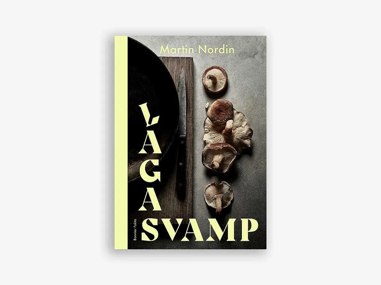 Boken "Laga svamp" av Martin Nordin visar en samling färska svampar, en kniv och en stekpanna. Perfekt för svamp mat-entusiaster.