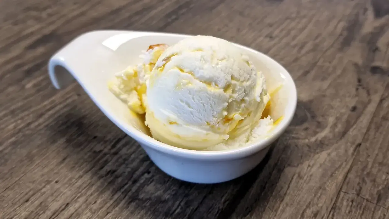 Ein cremiges Eis, das nach Buttermilch schmeckt, in einer weißen Schale auf Holztisch.