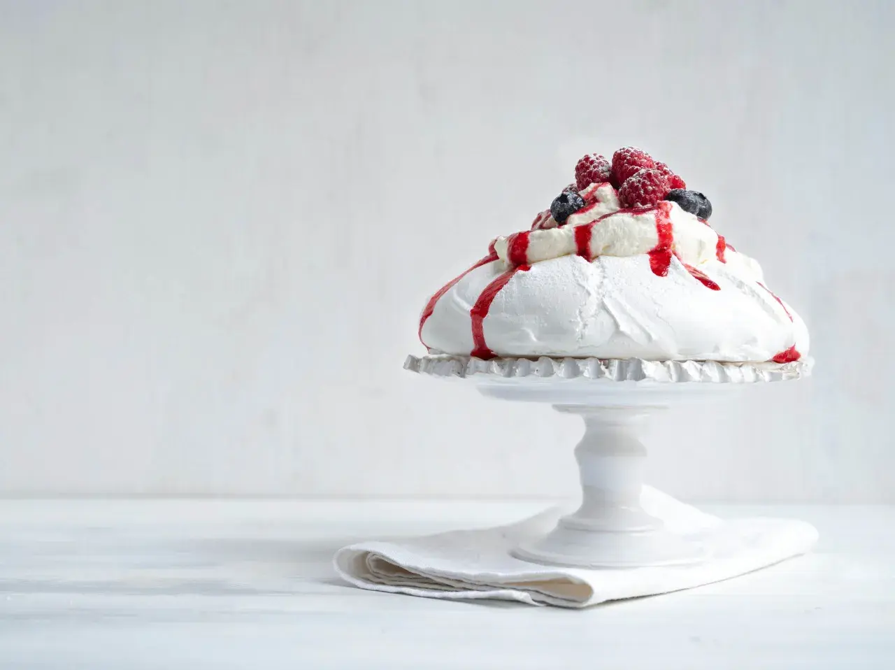 En vacker pavlova i långpanna, toppad med grädde, bär och röd sås.