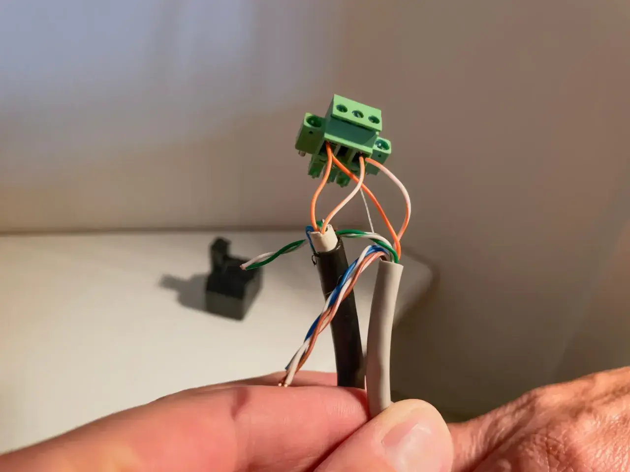 Connexion de fils électriques à un domino vert. Un câble noir et un câble gris sont dénudés, leurs fils colorés prêts pour le domino.