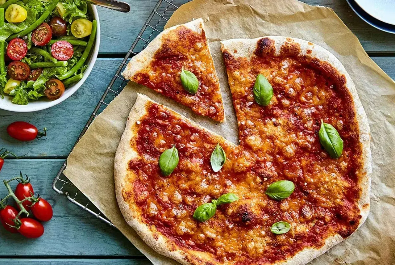 En nybakad liba pizza med tomatsås och basilika, serverad med en fräsch sallad.
