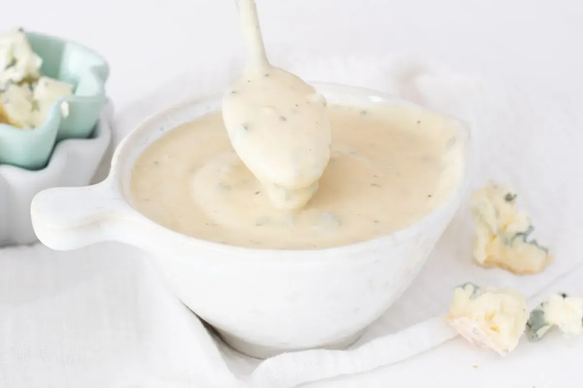Cremosa salsa gorgonzola servida en un cuenco blanco, con trozos de queso gorgonzola esparcidos alrededor.