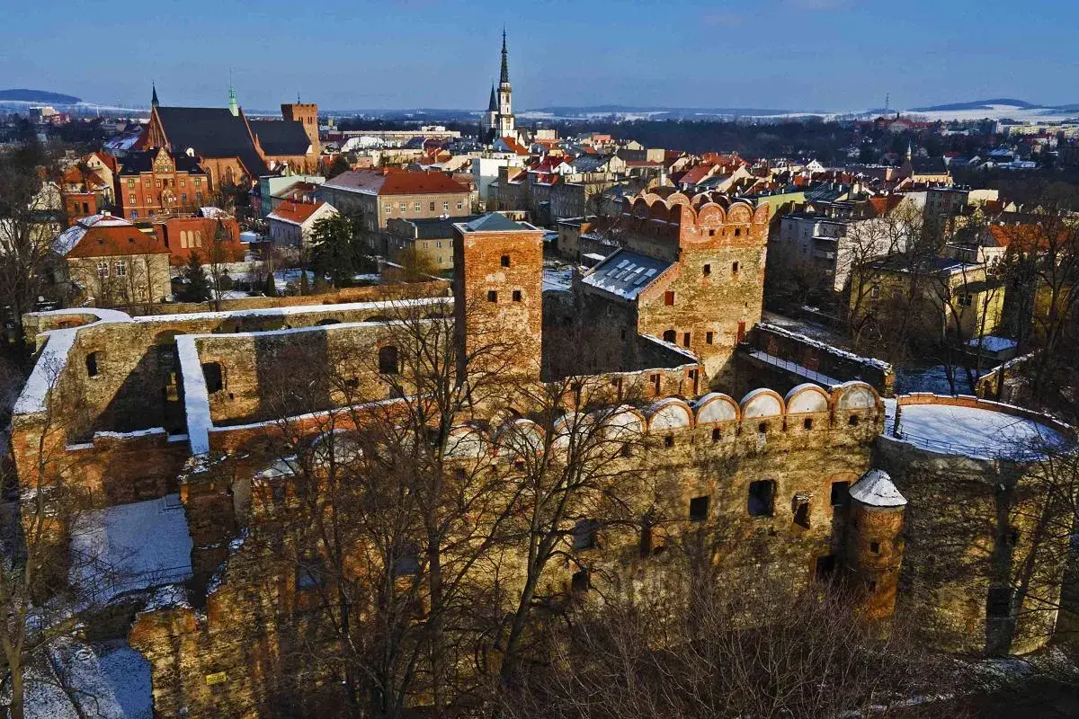 Ruiny zamku w Ząbkowicach Śląskich, z charakterystycznymi ceglanymi murami i wieżami, na tle zimowego krajobrazu miasta.