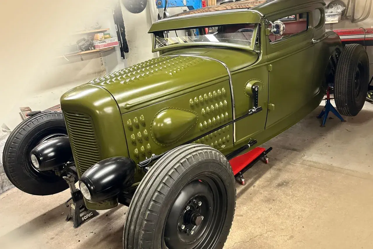 Grön hot rod, en klassisk bilbyggare USA, står på pallbockar i ett garage.
